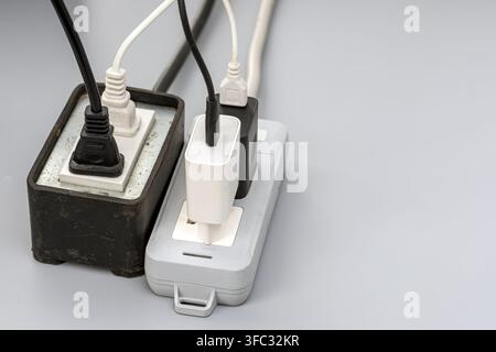 Overloaded power strips with tangled cords and chargers, highlighting electrical overload and fire hazard risks on a gray backdrop. Stock Photo