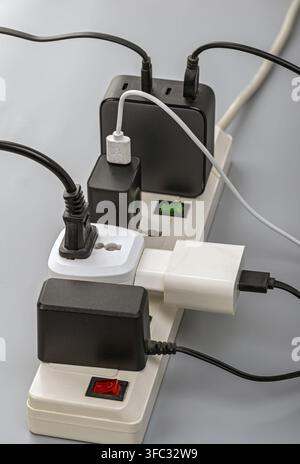 An overloaded power strip crammed with multiple chargers, adapters, and tangled cables plugged into limited outlets. Stock Photo