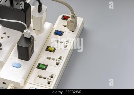 Overloaded power strip with multiple chargers and cables plugged into colorful switches, showing electrical safety risks. Stock Photo