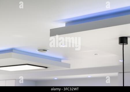 A contemporary ceiling features layered architectural elements with integrated lighting and subtle blue LED strips creating a sophisticated atmosphere Stock Photo