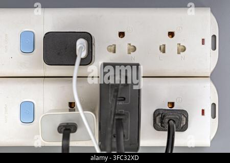 Close-up of a power strip with multiple outlets, blue switches, and various cables plugged in for charging devices. Stock Photo