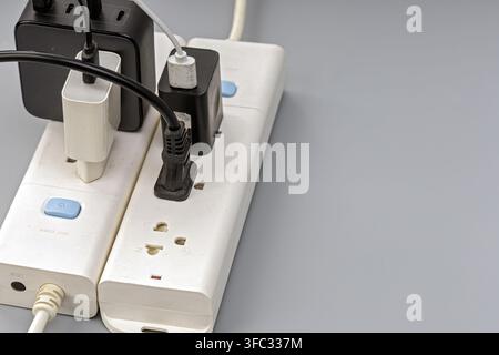 Overloaded power strip with multiple chargers and adapters plugged into outlets, showing risk of electrical overuse. Stock Photo