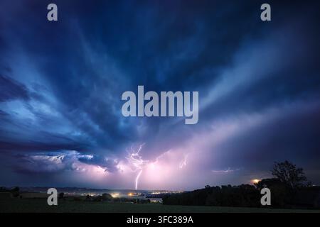Lightning bolt and clouds in dramatic dark blue night sky. A real natural weather photo of a thunderstorm. Stock Photo