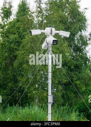 Multiple CCTV security cameras mounted on tall pole provide video surveillance and monitoring of an outdoor public area surrounded by greenery Stock Photo