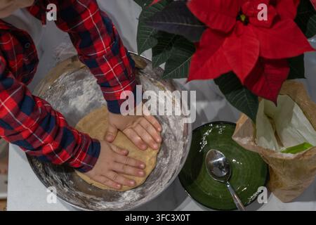 Child kneading homemade gingerbread dough by hand in a large mixing bowl while preparing Christmas cookies in a festive home kitchen. Top-down view of Stock Photo