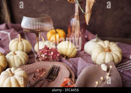 A rustic fall-inspired dining setup featuring white pumpkins, elegant plates, linen napkins, and a decorative goblet, perfect for Thanksgiving gatheri Stock Photo