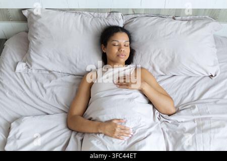 Black woman sleeping peacefully under soft bedding, illustrating healthy sleep Stock Photo