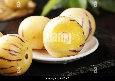 Pepino melons on a white plate with one cut open in a dark background. Stock Photo