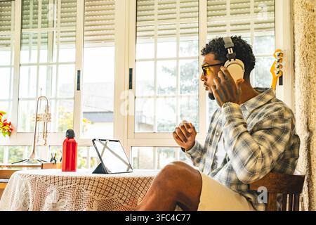 Young man wearing headphones and glasses sits beside bright window Stock Photo