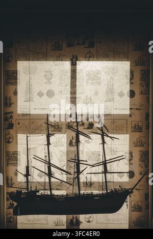 View of a detailed model ship silhouette displayed against a window with a vintage map-patterned curtain in Laane County, Estonia. Stock Photo