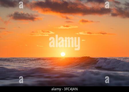 Bright setting sun over ocean waves during a fiery orange sunset Stock Photo