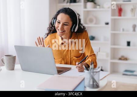 Smiling Hispanic Woman Working At Home Office, Engaging In Video Call With Laptop. Business Concept Stock Photo