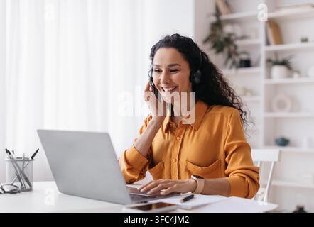 Smiling Hispanic Woman Wearing Headset Working On Laptop At Home Office, Business Concept Stock Photo