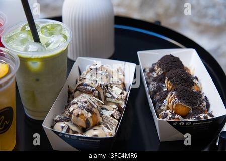 Trays of sweet dessert dough balls topped with chocolate sauce, crushed wafers, and cookie crumble served alongside iced matcha latte drinks Stock Photo