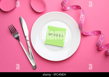 Paper note with word Anorexia, plate, cutlery and measuring tape on pink background, flat lay Stock Photo