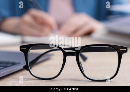 Keywords. Glasses on table and woman writing in notebook, selective focus Stock Photo