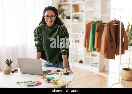 Smiling Hispanic Woman Working In Modern Office At Laptop, Fashion Design Concept Stock Photo