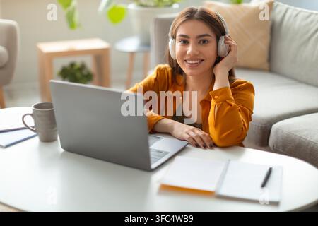 Smiling Young Hispanic Woman Wearing Headphones Working On Laptop At Home Office Stock Photo