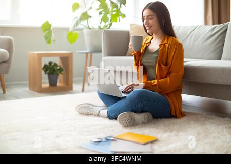 Happy Young Woman Sitting On Floor Working On Laptop With Coffee At Home, Lifestyle Concept Stock Photo