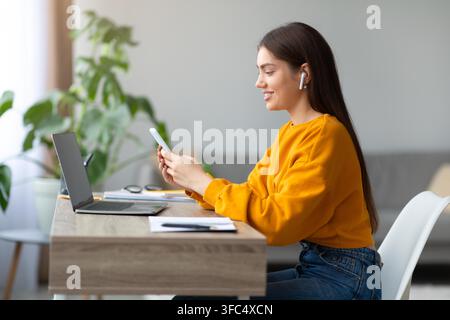 Young Woman With Long Hair Using Smartphone And Laptop At Home Office, Focused Stock Photo