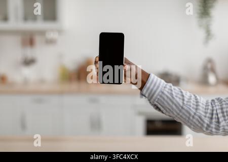 Unrecognizable Black Hand Holding Smartphone Displaying Blank Screen In Kitchen Stock Photo