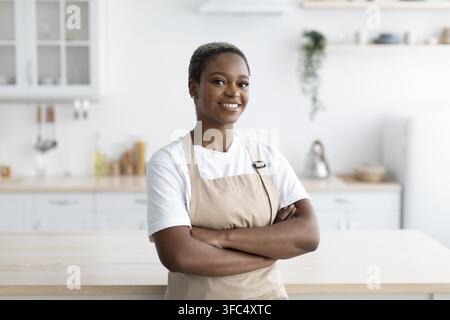 Smiling Black Woman Chef Standing With Arms Crossed In Modern Kitchen, Cooking Concept Stock Photo