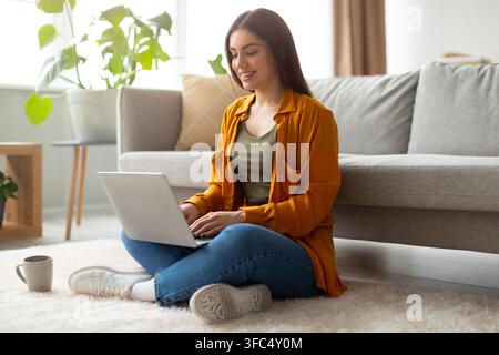 Happy Young Hispanic Woman Working On Laptop Sitting On Floor, Home Office Concept Stock Photo