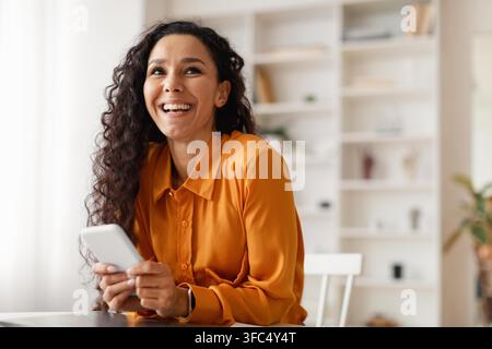 Smiling Young Mixed Race Woman Using Smartphone In Contemporary Office Environment Stock Photo