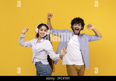 Happy Young Multiracial Couple Dancing With Headphones, Joyful Emotion, Yellow Background Stock Photo