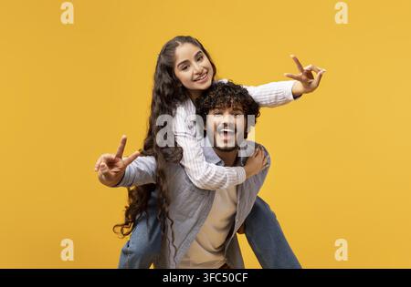 Happy Young Caucasian Couple Taking Fun Selfie, Yellow Background, Playful Gesture Stock Photo