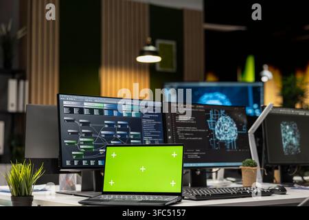 Green screen mockup laptop on startup office desk next to PC showing deep learning programming languages. Chroma key notebook in AI company workspace used for code testing and quality assurance Stock Photo