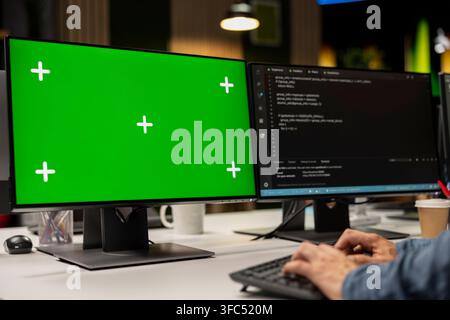 Technician using green screen PC to write code, debugging software issues and improving system stability. IT specialist in tech startup office typing on mockup computer keyboard Stock Photo