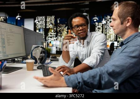Teamworking engineers talking in startup office, coding advanced machine learning models enhancing automation. Silicon Valley workplace colleagues doing brainstorming, using AI on computer at desk Stock Photo