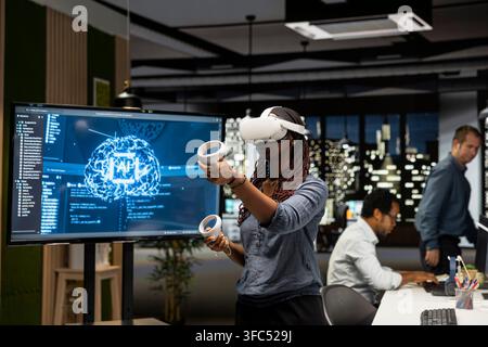 Programmer in tech startup office using VR headset and AI to automate repetitive tasks. Worker using virtual reality and artificial intelligence to speed up feature implementation Stock Photo