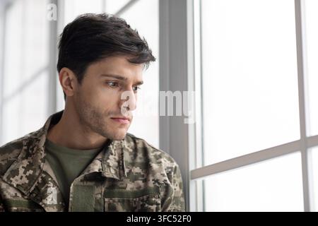 Thoughtful Young Man In Military Uniform Looking Out Of Window In Office Setting Stock Photo