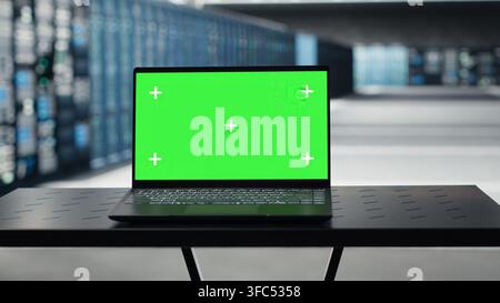 Green screen laptop in high tech data center facility with multiple rows of fully operational server racks. Mockup notebook used to oversee server hub built for digital storage systems Stock Photo