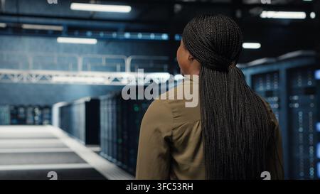 High tech data center technician uses tablet to develop disaster recovery plans, minimizing downtime. IT employee walking in server room, enhancing data protection protocols using device, camera B Stock Photo