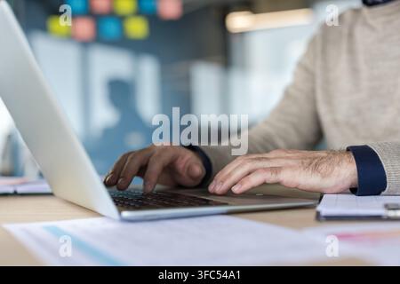 Business professional hands are typing on a laptop keyboard at a wooden desk, working efficiently in a modern office environment, demonstrating productivity and technology use Stock Photo