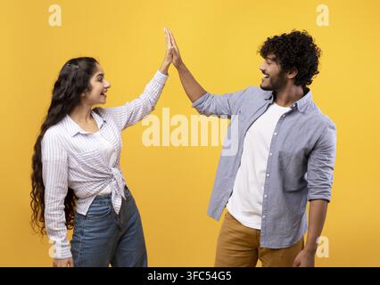 Happy South Asian Couple Giving High Five Together, Joyful Expression, Yellow Background Stock Photo