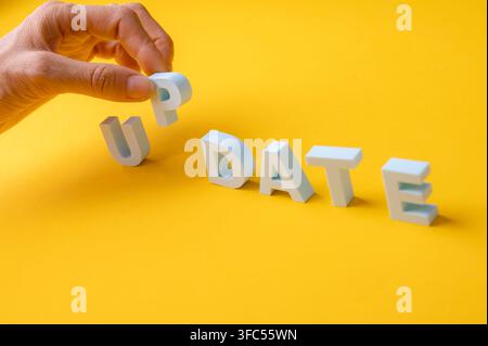 Human hand completing the word UPDATE with white 3D letters on a yellow background. Concept of updating, upgrading, software and system updates, new v Stock Photo