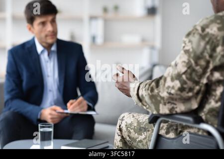 Male Caucasian Therapist Taking Notes During Consultation With Black Male Soldier, Healthcare Concept Stock Photo