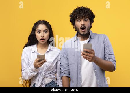 Surprised Young Couple Reacting To News, Holding Smartphones, Studio Setting Stock Photo