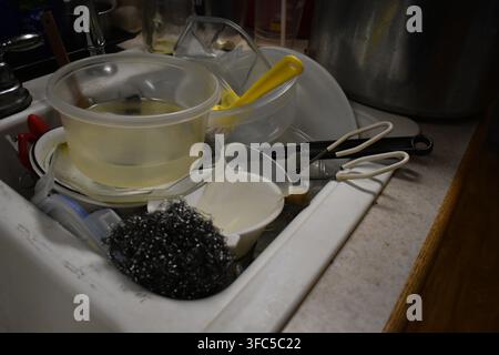 A white porcelain sink full and overflowing with dirty dishes. Stock Photo