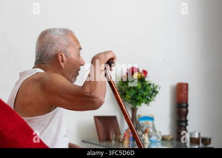 Elderly man using cane to stand up with effort showing mobility struggle and physical limitation at home Stock Photo