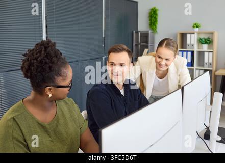 Smiling coworkers collaborating at computers in modern office, business teamwork Stock Photo