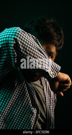 A distressed thirty two year old Asian male model aggressively covers a fearful face with one raised arm against a heavy dark studio background. Inten Stock Photo