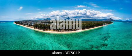 Aerial view of a tropical coastline with turquoise water, a sandy beach, lush trees, and distant mountains in France. Stock Photo