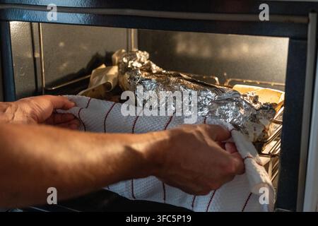 Close-up of a whole fish baking in the oven on aluminum foil with lemon slices and onions. Homemade seafood preparation scene showing a cooked fish be Stock Photo