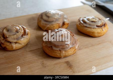 Close-up of homemade cinnamon rolls topped with sweet icing and arranged on a wooden cutting board. Freshly baked golden pastries with visible cinnamo Stock Photo