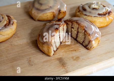 Close-up of a freshly baked cinnamon roll cut open to reveal the soft layered interior and cinnamon swirl. Homemade glazed pastries are arranged on a Stock Photo